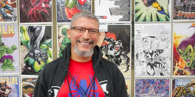 A man with grey hair poses infront of a wall of art.