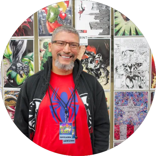 A man with grey hair named Spider poses infront of a wall of art.