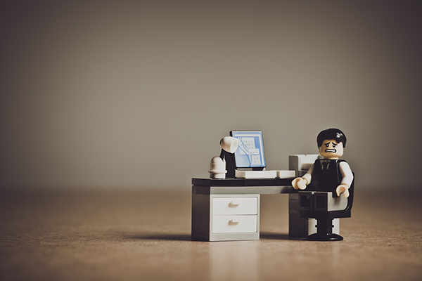 a small lego figure infront of a lego computer desk looking very stressed